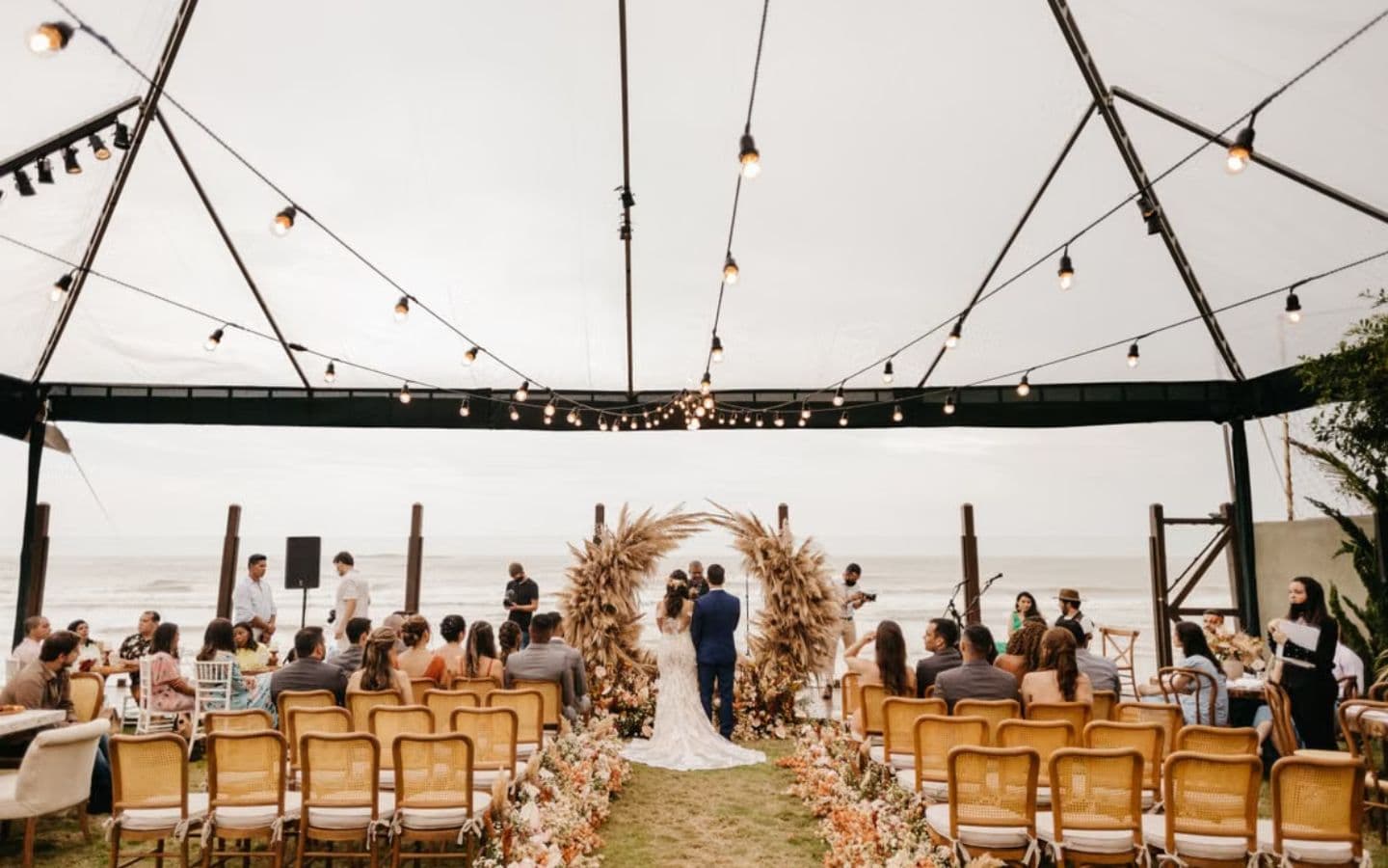 A beachfront wedding ceremony under a marquee strung with lights