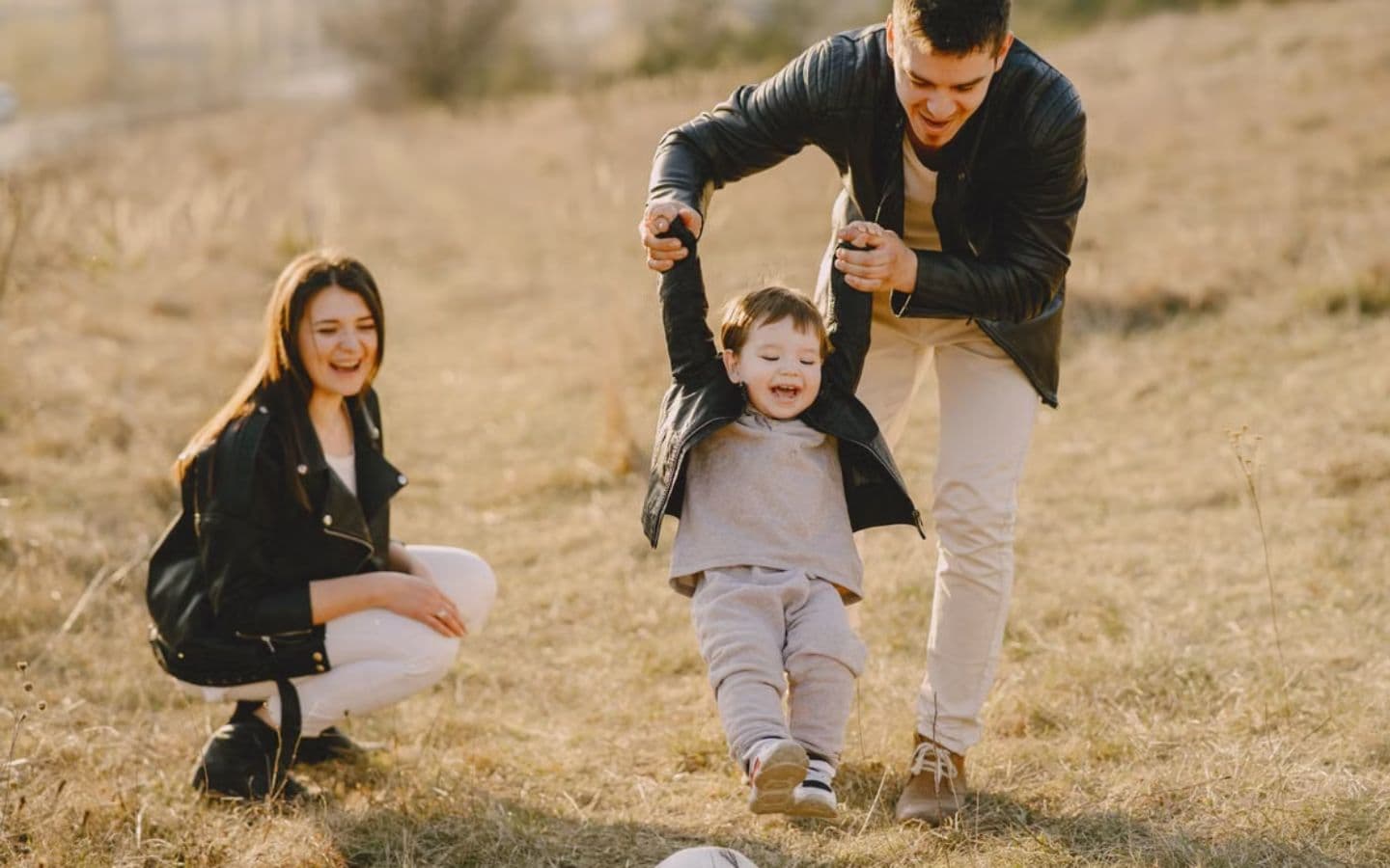 Parents swinging their small child between them in a field at golden hour