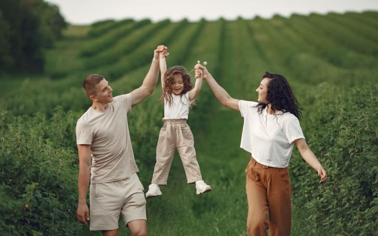 A family lifting their daughter by the hands while walking through a green field